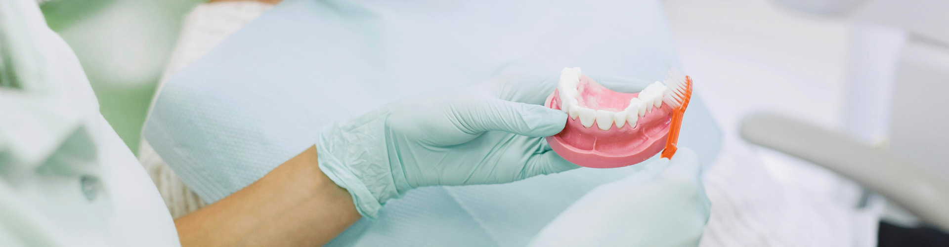 Gloved hands demonstrating teeth brushing on denture model.